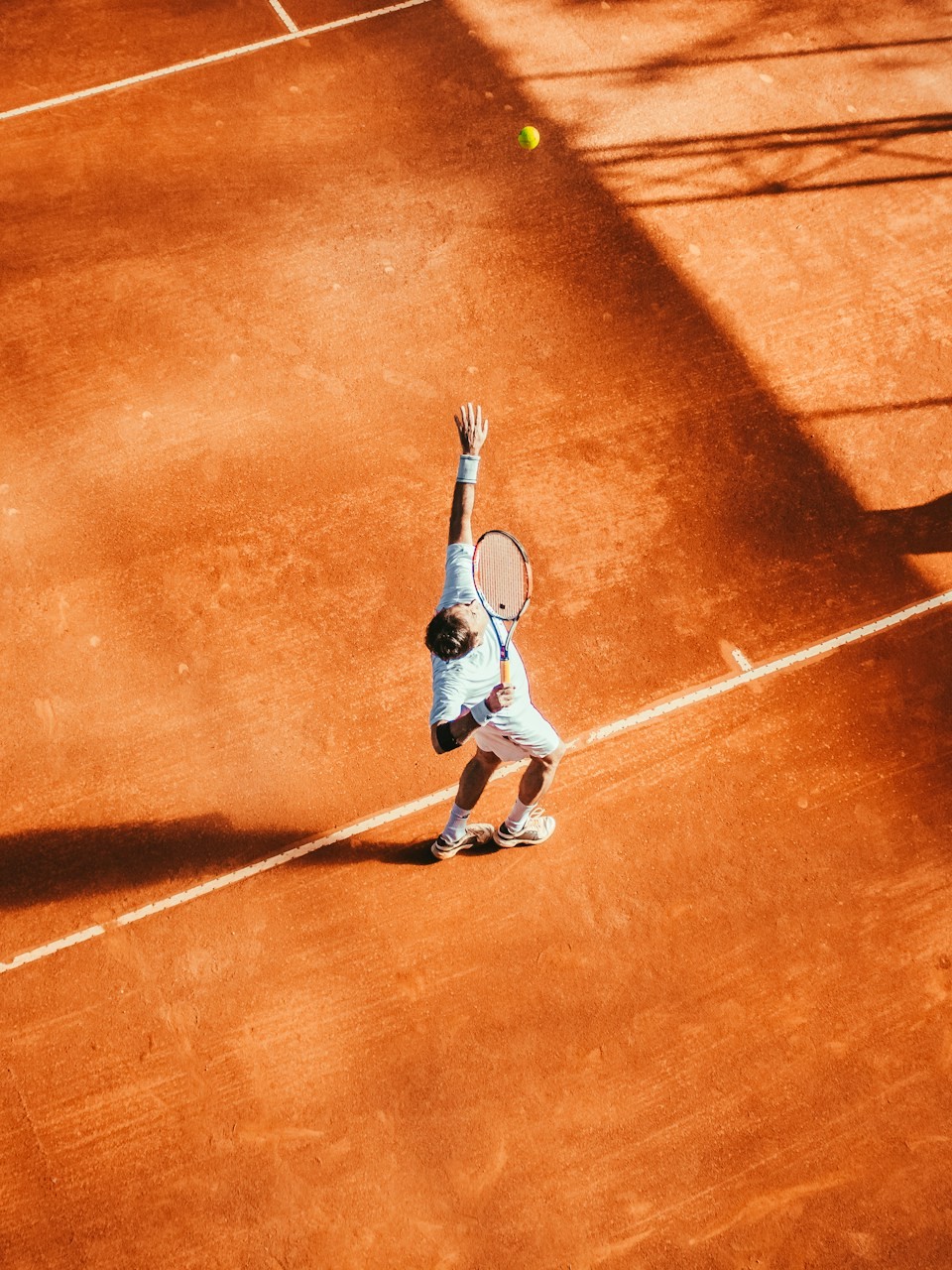 Tennisspieler beim Aufschlag auf dem Sandplatz – Vereinsapp für Tennisvereine